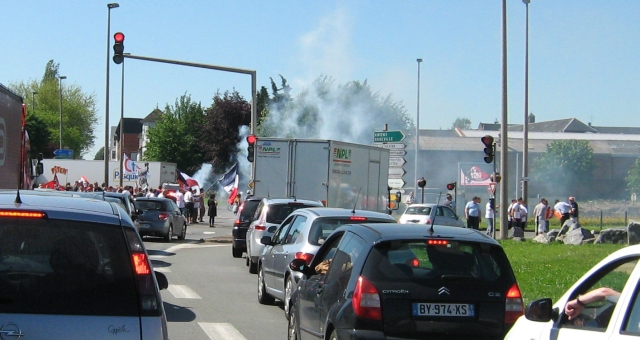 lines of traffic in the distance protestors with smoking flares and banners in arras